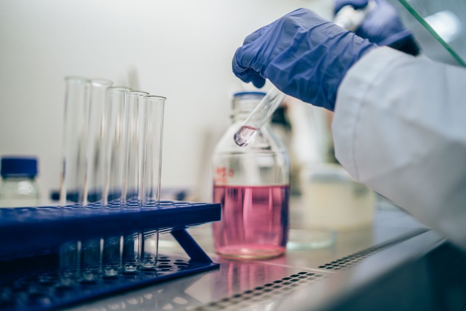 Científico en laboratorio manipulando un tubo de ensayo con líquido rosa para investigación científica.