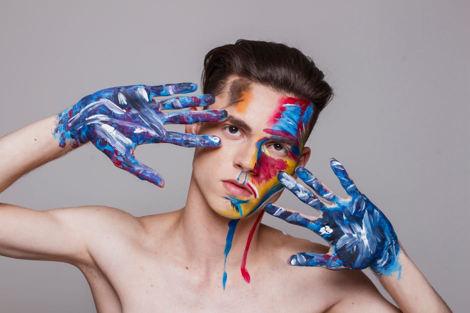 Retrato artístico vibrante de un hombre con la cara y las manos pintadas en colores brillantes, mostrando creatividad y expresión.