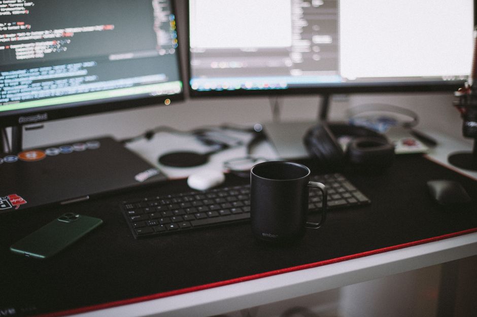 Configuración de oficina en casa acogedora con monitores dobles, un teclado y una taza de cerámica negra.