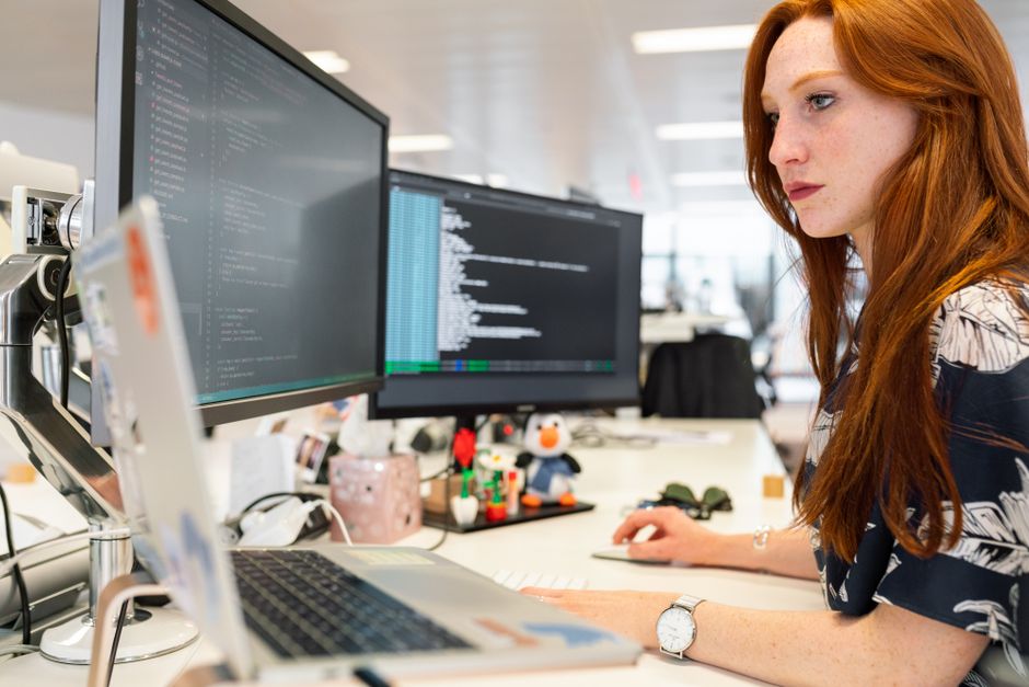 Una ingeniera de software femenina concentrada programando en monitores duales en una oficina moderna.