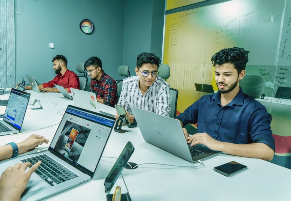 Grupo de jóvenes profesionales trabajando juntos en un entorno de oficina moderno, utilizando laptops y tecnología.