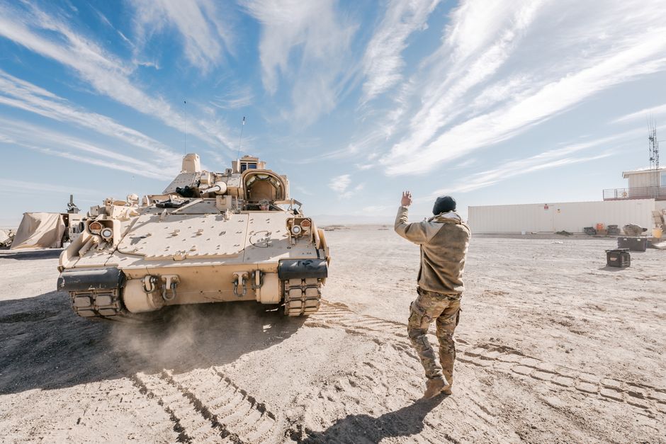 Vehículo de Combate Bradley y soldado en operación de entrenamiento en el desierto bajo un cielo despejado.