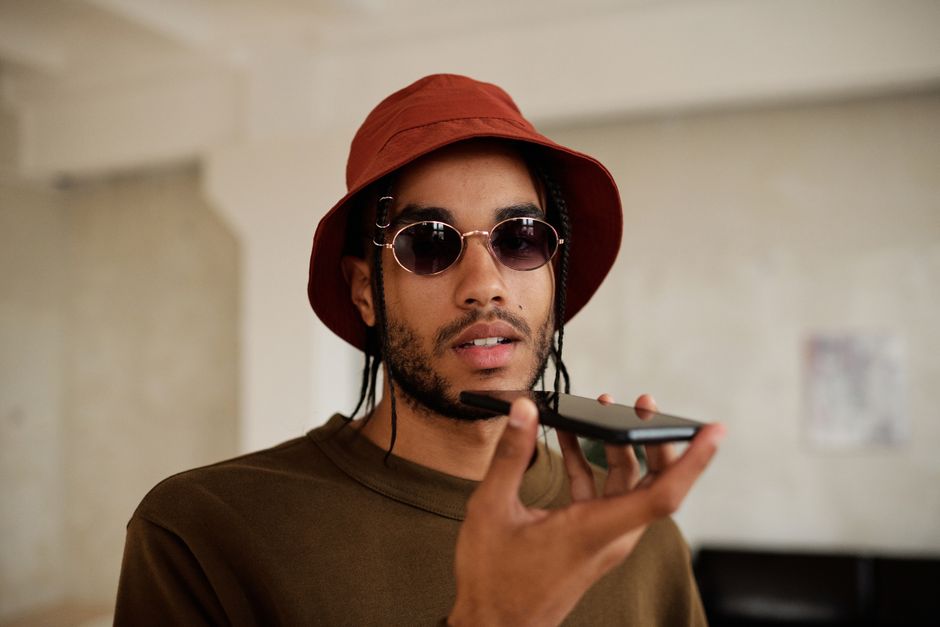 Hombre a la moda con gafas de sol y un sombrero de cubo hablando por un smartphone en interiores.