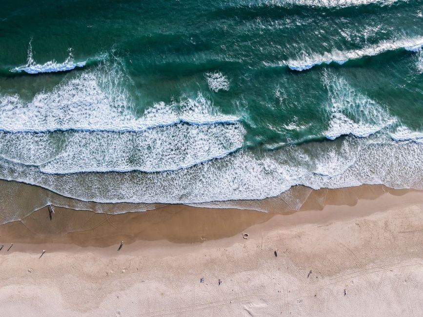Impresionante toma aérea de olas del océano golpeando una orilla arenosa en un día despejado.
