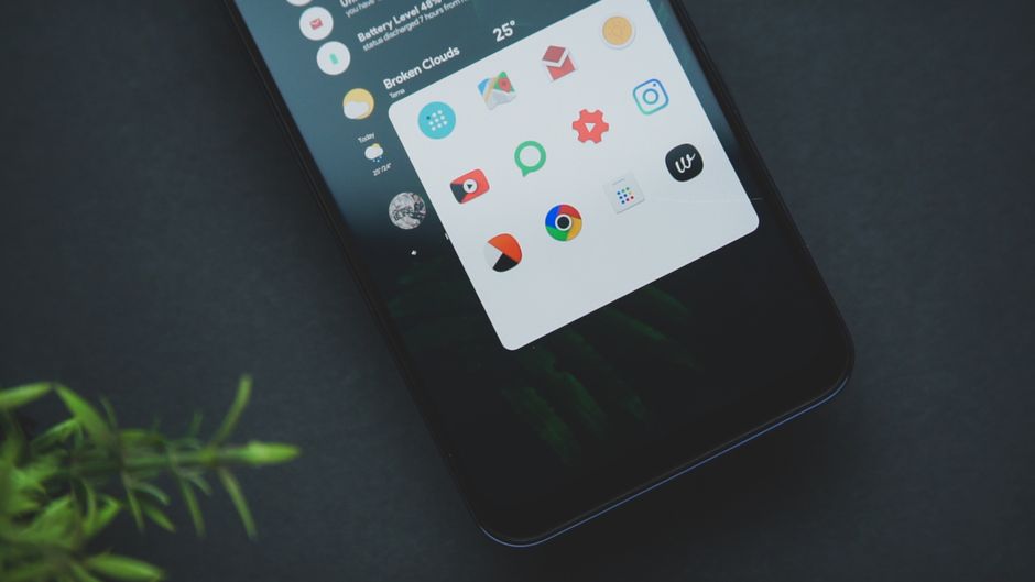 Primer plano de un teléfono inteligente que muestra varios íconos de aplicaciones sobre un fondo oscuro con vegetación.