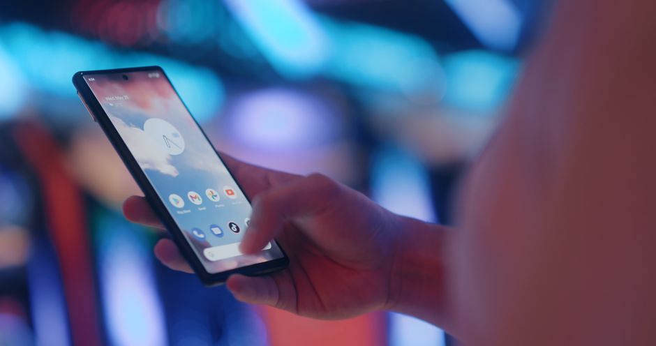Una mano sostiene un smartphone mostrando aplicaciones, resaltadas por luces de neón vibrantes.