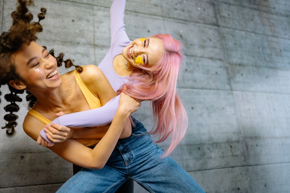 Dos mujeres jóvenes riendo y posando con peinados y maquillaje creativos.
