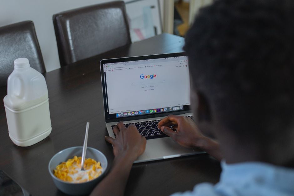 Una persona navegando por Google en un portátil mientras toma su desayuno de cereales en la mesa.