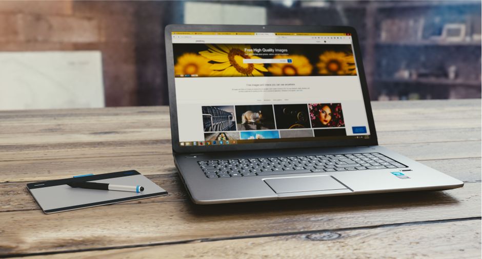 Portátil con página web abierta en un escritorio de madera, acompañado de una tableta y un bolígrafo, representando una configuración de trabajo digital.