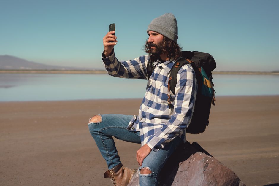 Hombre casual con traje moderno se toma un selfie durante una aventura al aire libre junto a un lago.