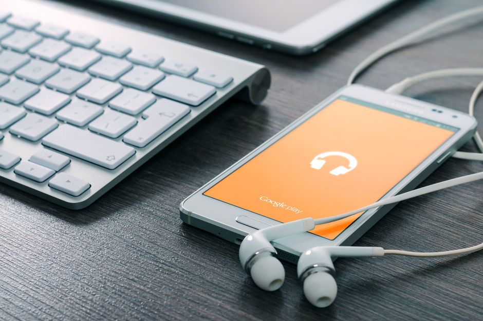 Un smartphone con auriculares conectados junto a un teclado en un escritorio de madera, mostrando tecnología moderna.