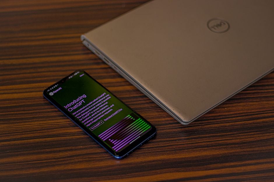 Un smartphone mostrando la aplicación ChatGPT junto a un portátil cerrado sobre una mesa de madera.
