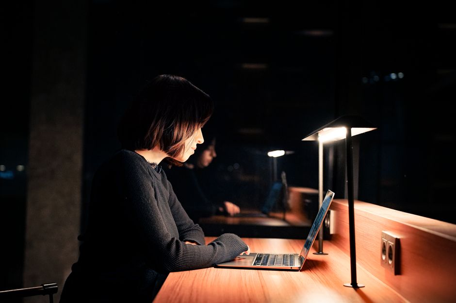 Una mujer concentrada en su portátil en un escritorio con iluminación tenue, trabajando tarde en la noche.