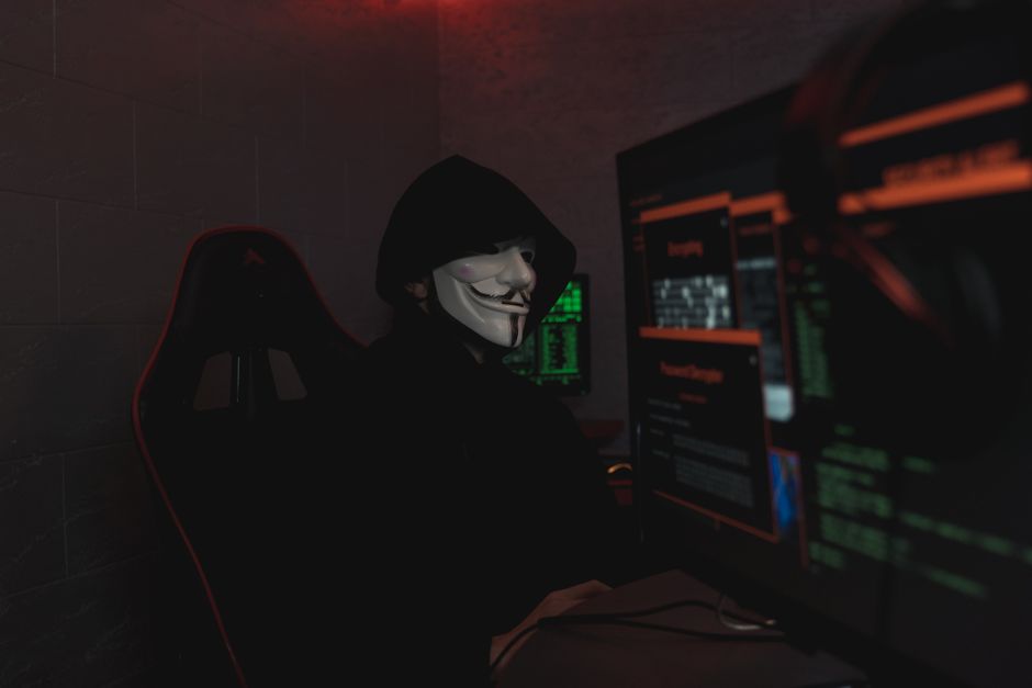 Un hacker anónimo con máscara trabajando en una computadora en una habitación oscura.