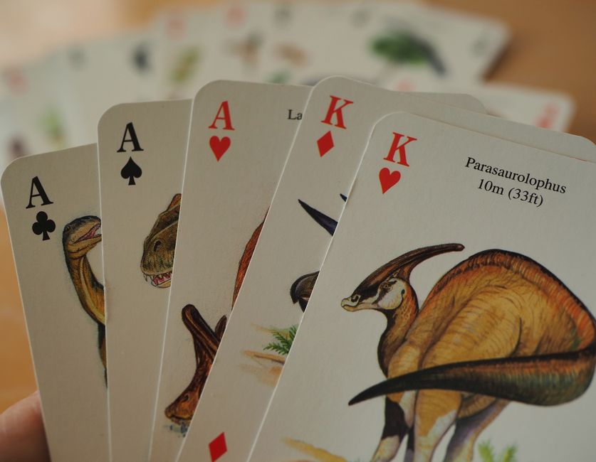 Primer plano de cartas de juego con temática de dinosaurios que presentan ases y reyes en una mano de póquer.