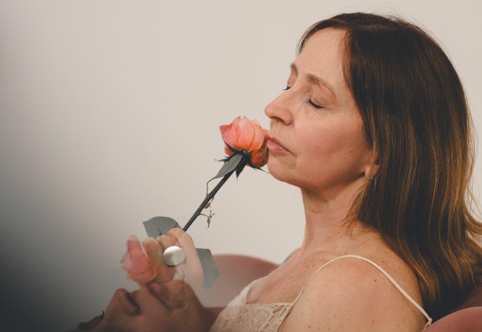 Una mujer serena disfruta del aroma de una rosa rosa en el interior de su casa, capturando un momento de tranquilidad.