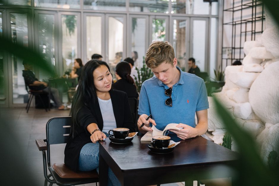 Una joven pareja se sienta en una mesa de café, disfrutando de café y leyendo juntos.