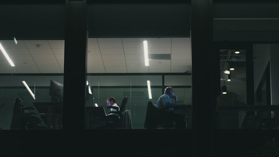 Dos personas trabajando hasta tarde en un moderno edificio de oficinas de Houston, visibles a través de una ventana.