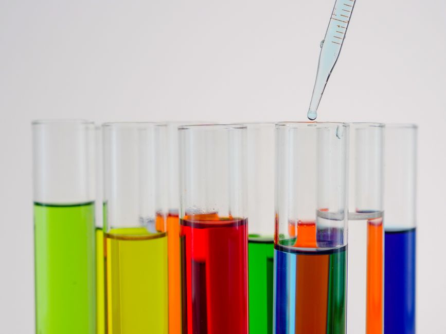 Primer plano de líquido colorido en tubos de ensayo con una pipeta de goteo en un entorno de laboratorio.