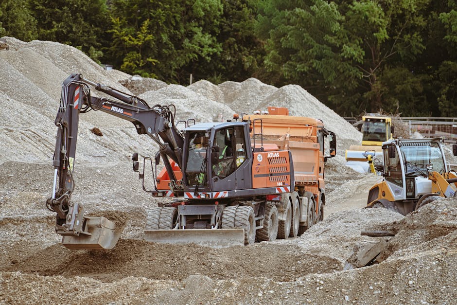 Excavadora y maquinaria en un sitio de construcción concurrido con montones de arena.