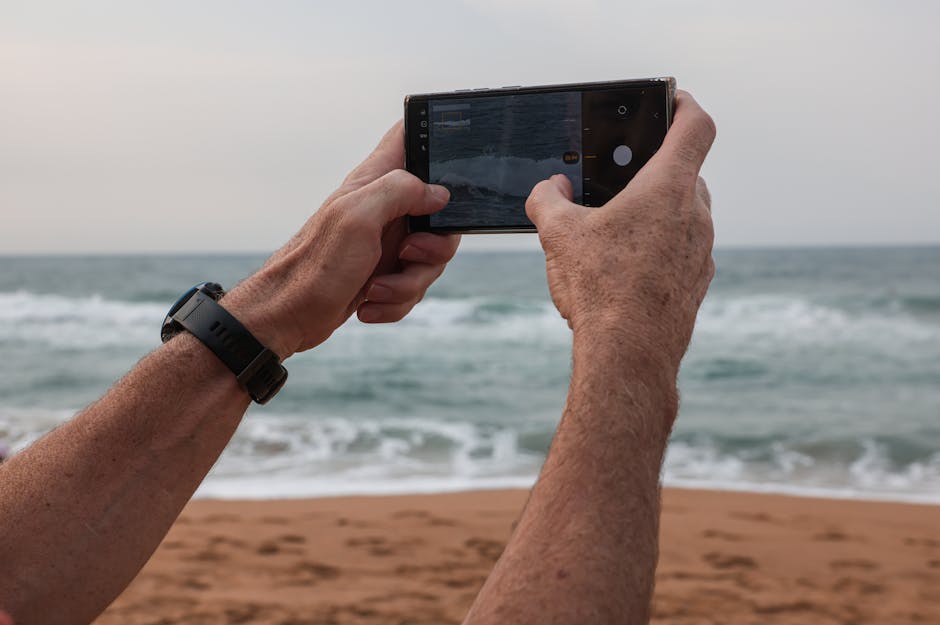 Una persona toma una fotografía de las olas del océano con un teléfono inteligente en una playa de arena.
