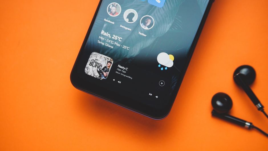Primer plano de un smartphone con auriculares sobre un fondo naranja mostrando una lista de reproducción y una actualización del clima.