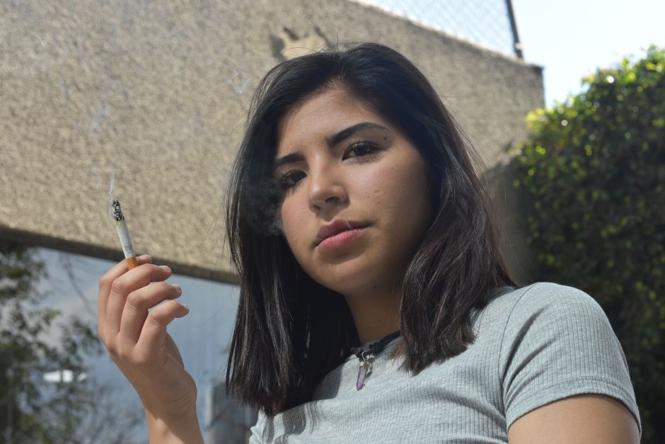 Retrato de una joven con un cigarrillo al aire libre, que irradia una atmósfera relajada e introspectiva.