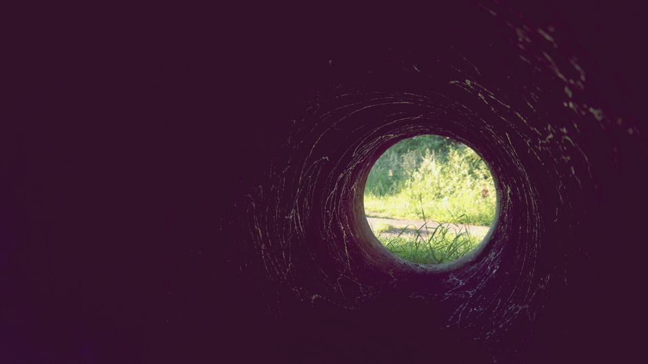 Una vista a través de un túnel oscuro con la luz del sol iluminando la hierba afuera.