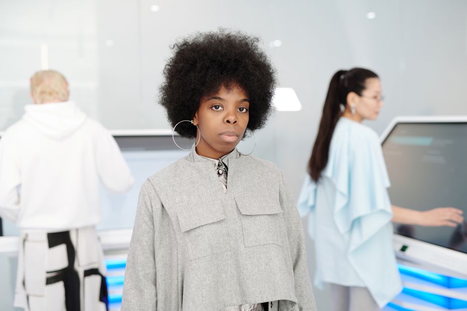 Mujer elegante con cabello afro se presenta con confianza en un entorno interior futurista.