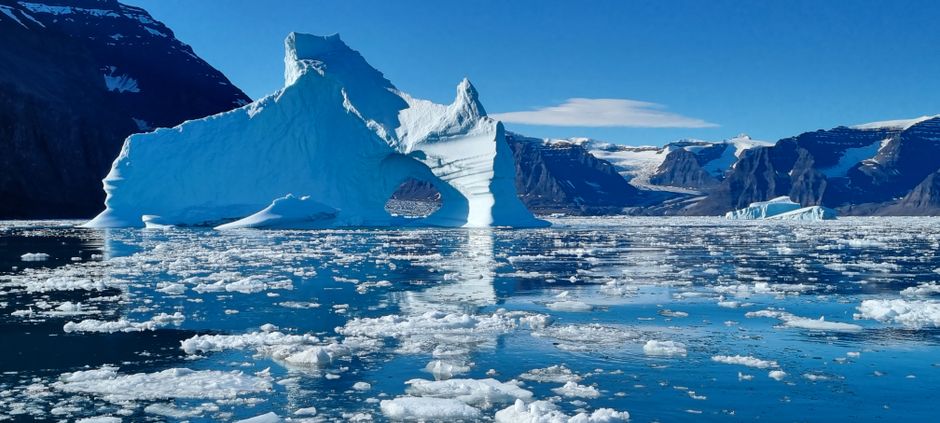 Majestuoso iceberg flotando en aguas heladas con montañas al fondo.