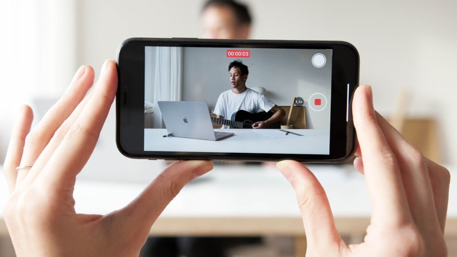 Hombre tocando la guitarra mientras graba un vídeo para su vlog usando un smartphone.