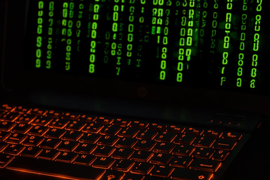 Un teclado de portátil con retroiluminación naranja que muestra símbolos de código digital verdes.