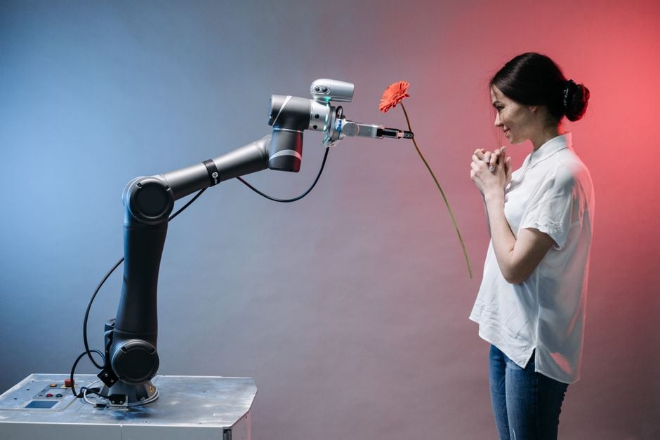 Un brazo robótico ofrece una flor a una mujer en una exhibición de tecnología y conexión humana.