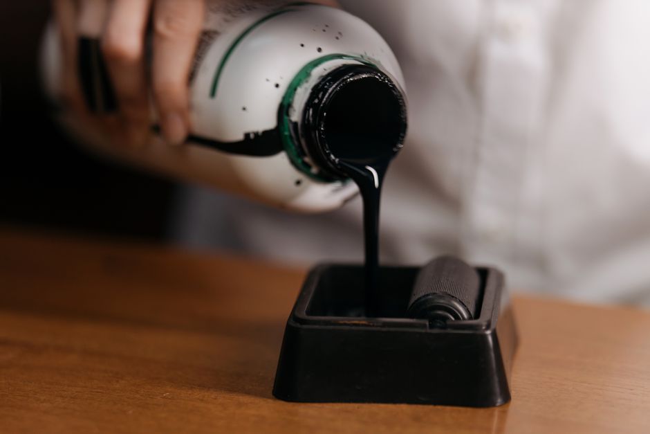Una imagen en primer plano de tinta de una botella siendo vertida sobre un rodillo, resaltando suministros de arte.