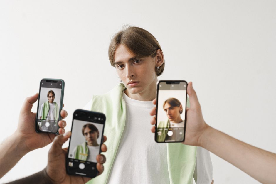 Un hombre con una camisa blanca está siendo fotografiado con varios teléfonos inteligentes contra un fondo simple.