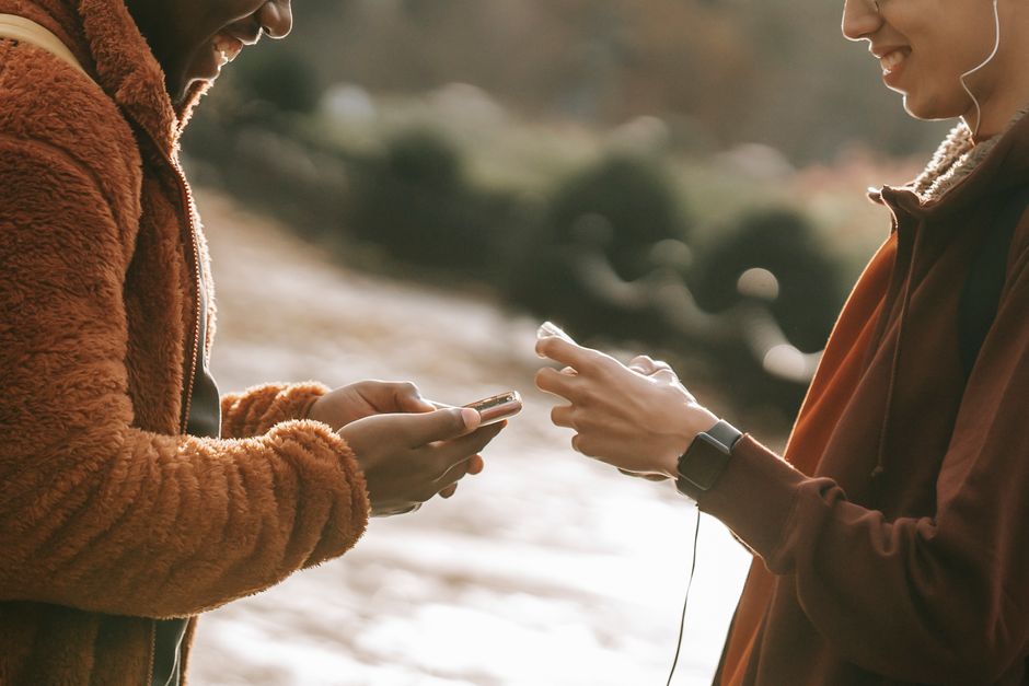 Dos amigos interactuando al aire libre, usando smartphones en un ambiente alegre y relajado.