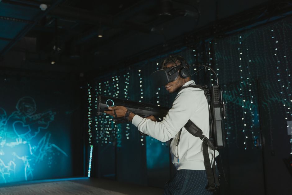 Hombre adulto comprometido en juegos de realidad virtual con casco de VR y arma simulada.