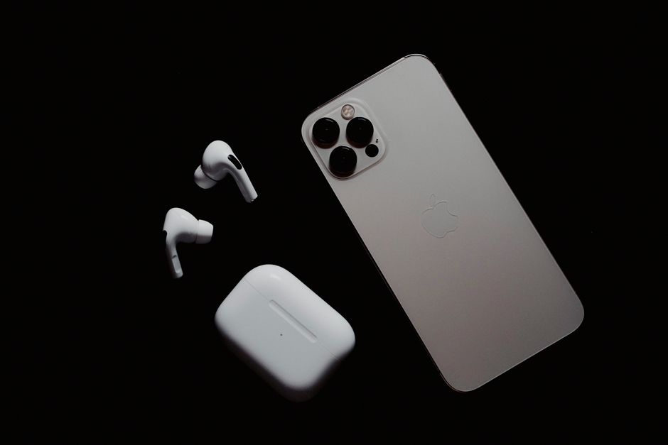 Primer plano de un smartphone y auriculares inalámbricos sobre una superficie oscura, mostrando gadgets tecnológicos modernos.