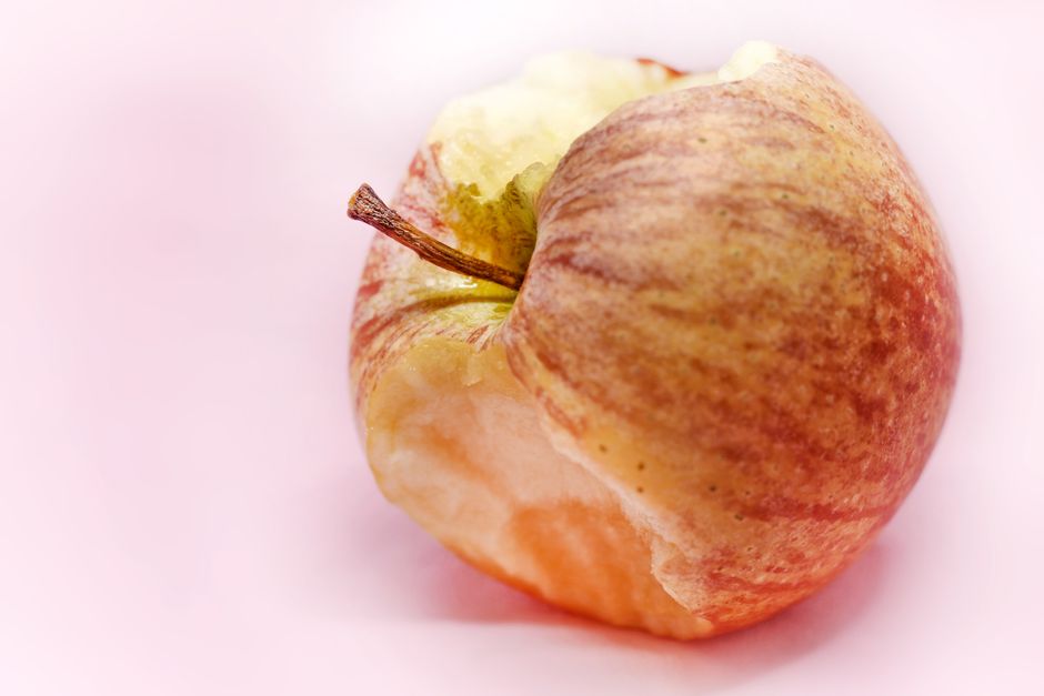 Una manzana mordida que muestra su textura fresca y crujiente sobre un fondo rosa suave.