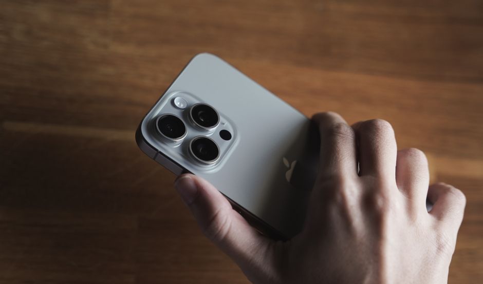 Primer plano detallado de la lente de la cámara de un smartphone sostenida en una mano humana, mostrando el diseño tecnológico.