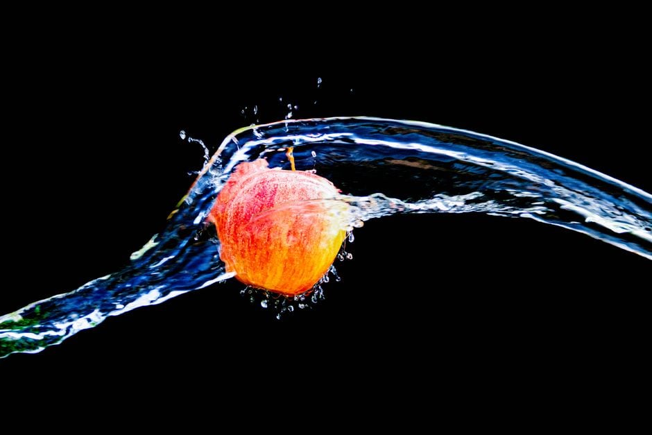 Una manzana vibrante sumergida en un splash de agua sobre un fondo negro.