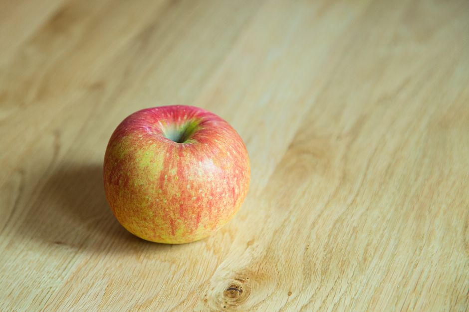 Una manzana roja madura descansando sobre una superficie de madera, perfecta para conceptos de alimentación saludable.