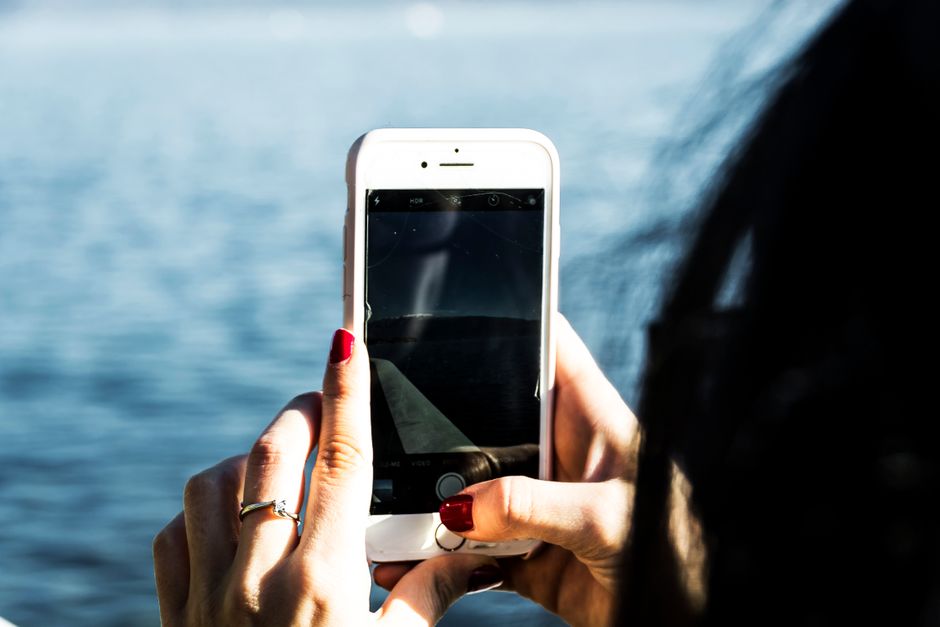 Primer plano de una persona fotografiando un lago sereno con un smartphone, mostrando la tecnología en la naturaleza.