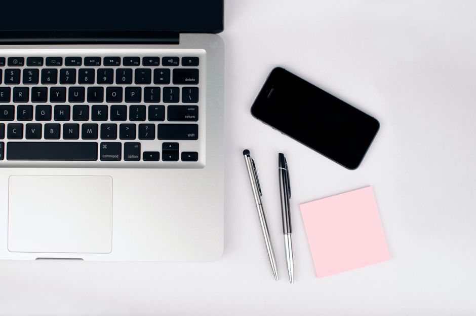 Vista superior de un espacio de trabajo elegante con un portátil, teléfono inteligente y artículos de oficina sobre un escritorio blanco.