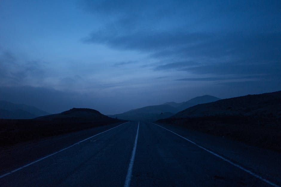 Tranquilo camino montañoso bajo un cielo azul crepuscular, que evoca una sensación de paz y viaje sin fin.