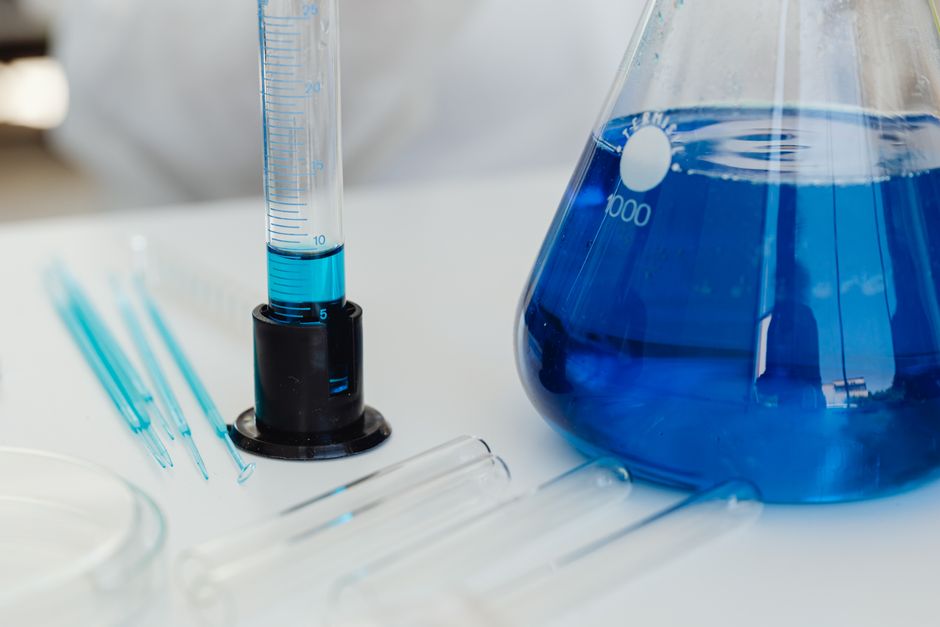 Primer plano detallado de equipos de laboratorio incluyendo tubos de ensayo y matraz de Erlenmeyer con líquido azul.