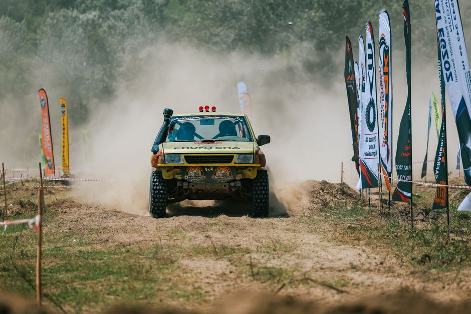Escena dinámica de carrera todoterreno con un vehículo levantando polvo entre banderas y espectadores.