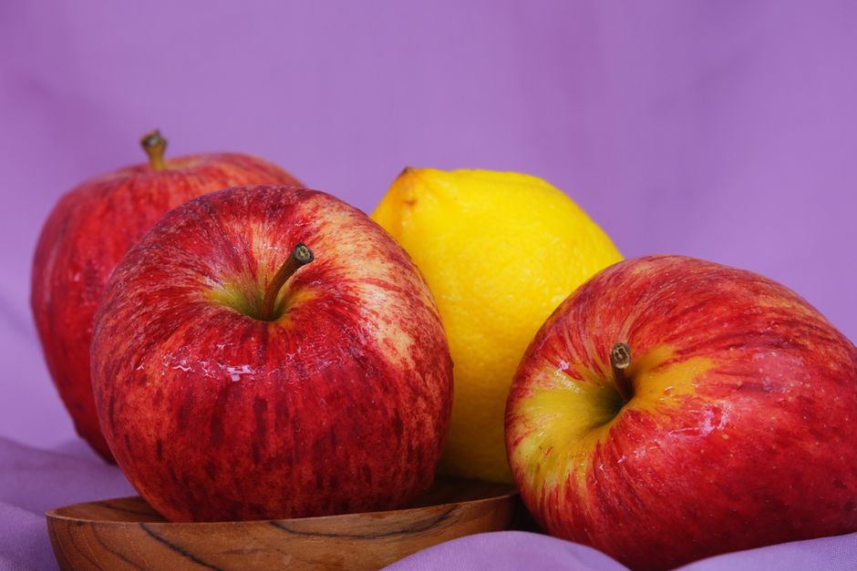 Tres manzanas rojas frescas y un limón sobre un fondo morado vibrante para un contraste de color.