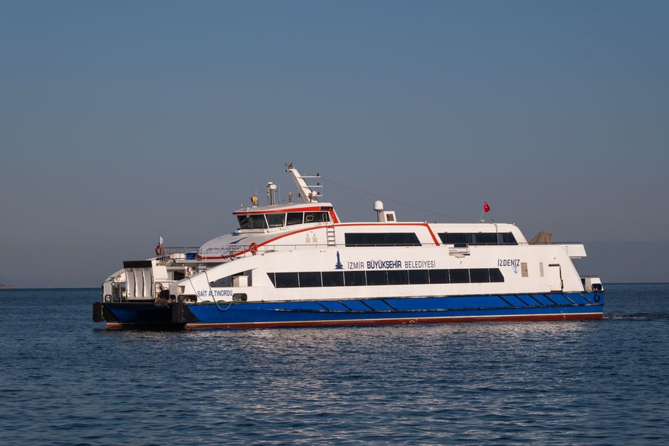 Un barco ferry deslizándose por las tranquilas aguas de İzmir, Turquía, bajo cielos despejados.