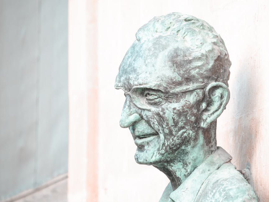 Busto de bronce esculpido de un anciano con gafas, que muestra detalles desgastados y un estilo de arte clásico.